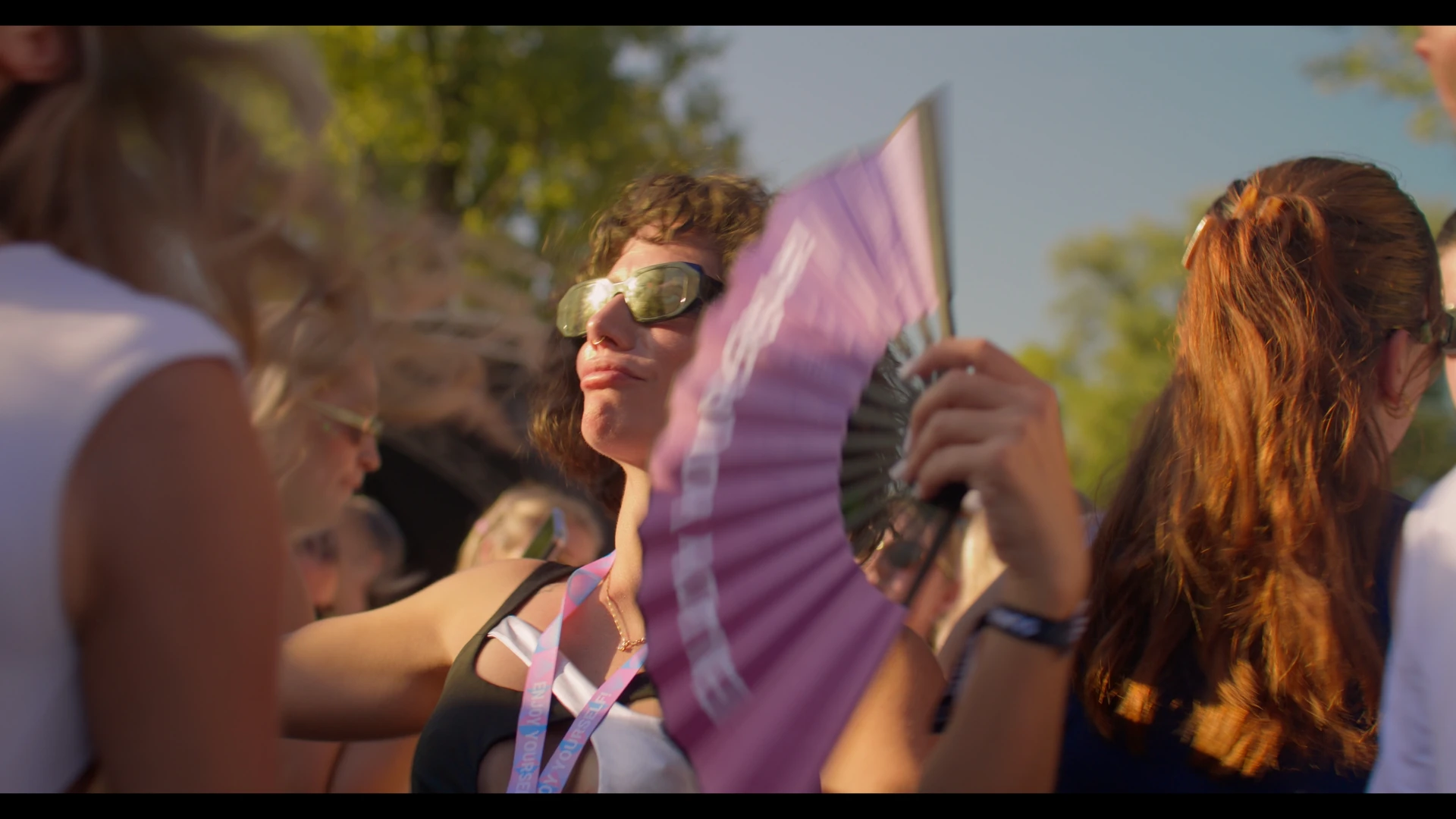 A festival guest with sunglasses and a purple fan, captured in warm evening light.